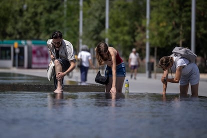 Tres personas se remojan piernas y brazos con agua en una fuente ornamental del parque de Glòries de Barcelona, este viernes.