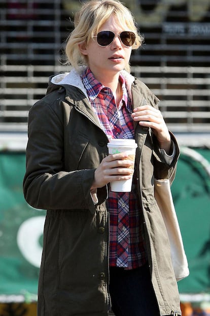 Michelle Williams, con parka militar, camisa de cuadros y jeans, tomándose un café por las calles de Brooklyn.