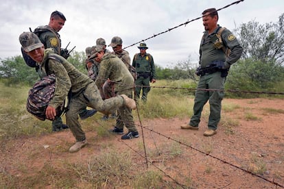 Los cinco migrantes atraviesan una reja de púas vigilados por los agentes.