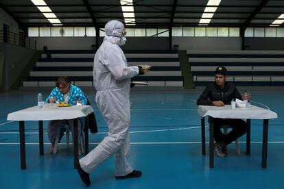 Un trabajador del 'catering' de la asociación AIXIÑA sirve comida a Elena Marmoloc, de 50 años, y a Jamali Abderrazak, dos personas sin hogar que ha dado positivo en covid-19, durante su estancia en el polideportivo de Oira, habilitado por el Ayuntamiento de Orense para este fin.