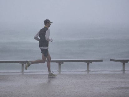 Un ‘runner’ corre bajo una intensa lluvia junto al mar, en el litoral de Barcelona.
