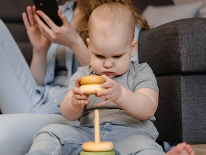 Una madre mira su móvil mientras su hijo juega.