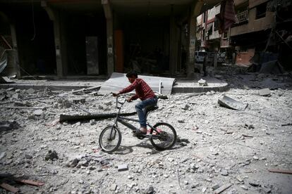 Un niño juega con su bicicleta por una calle destruida en la ciudad siria de Duma, el 27 de marzo de 2017.