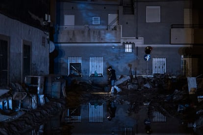 Un vecino de la localidad  Massanassa (Valencia) se abre paso de noche en una calle cubierta de barro y escombros, iluminándose con la luz de un frontal, el 4 de noviembre . Las fachadas de las casas apenas se distinguen bajo el tenue reflejo de las luces de los vehículos de emergencias. 