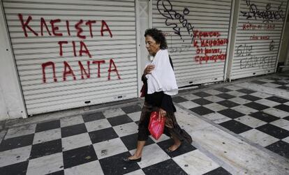 Una mujer camina junto a una tienda cerrada en cuya persiana se puede leer "Cerrado para Siempre", en el centro de Atenas.