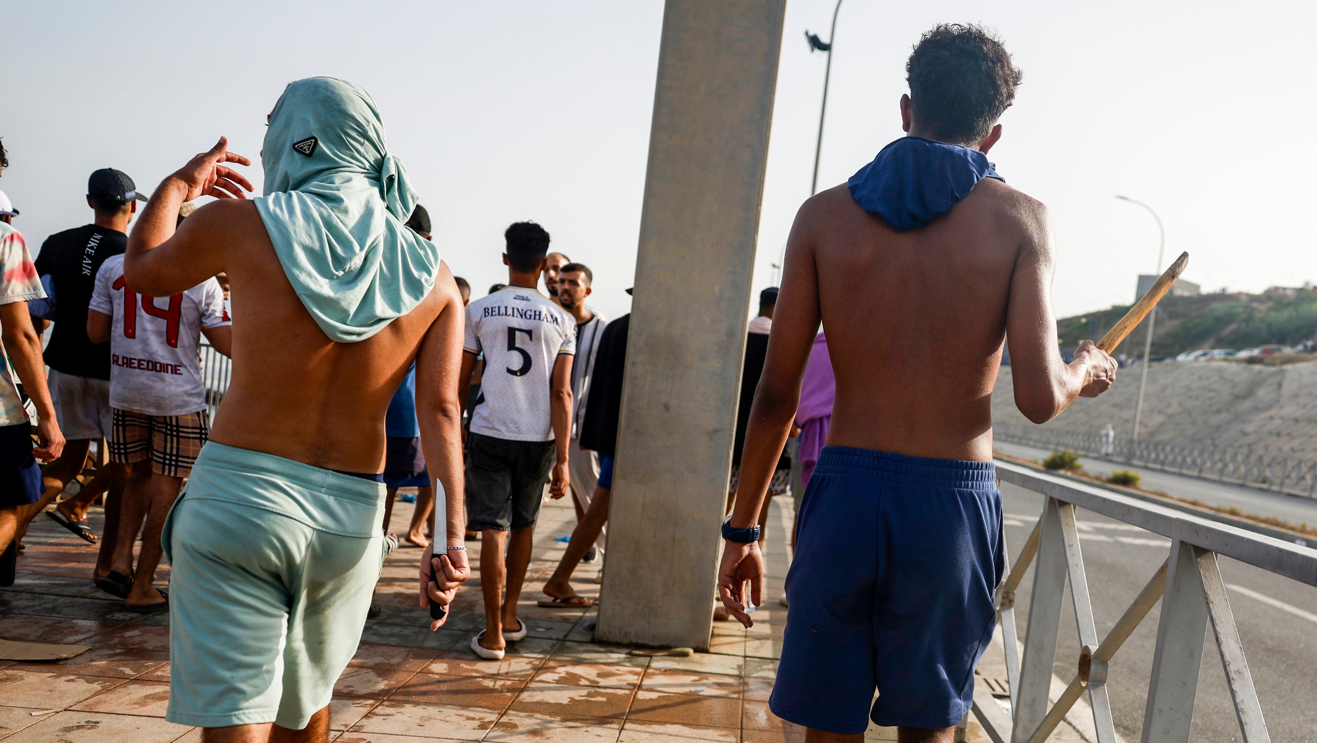 Dos hombres armados con un cuchillo (izquierda) y un palo siguen en Ceuta a un grupo de inmigrantes hacia la frontera con Marruecos el pasado día 31.