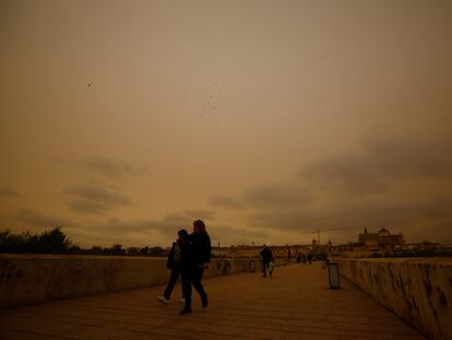 GRAFAND6950. CÓRDOBA, 15/03/2022.- Varias personas caminan por el Puente Romano de Córdoba con cielo cubierto por la calima, hoy martes cuando un excepcional episodio de polvo procedente del desierto del Sáhara ha penetrado en la Península y Baleares, y ha teñido de rojo los cielos de la costa mediterránea, en Andalucía especialmente en Jaén y Almería, donde la calima no se registraba con esta intensidad desde hacía varias décadas. EFE/Salas
