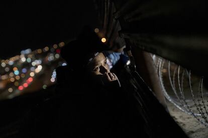 Un migrante mira a través de un agujero en la valla, mientras buscan un lugar para cruzar la frontera de Estados Unidos.