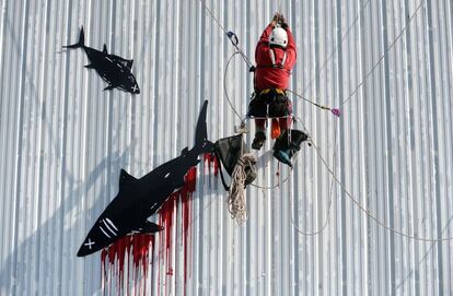 Un activista de Greenpeace colorea con pintura roja un logotipo de atún en un edificio de conservas como protesta contra los métodos de pesca en Douarnenez, Francia.
