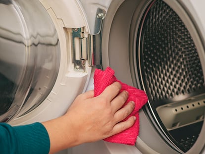 Una persona limpiando una lavadora con un trapo.
