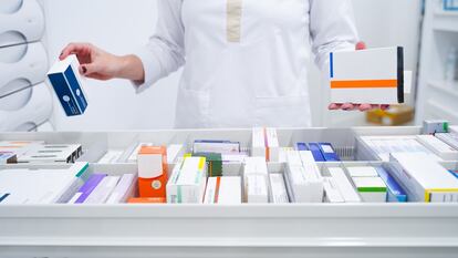 Una farmacéutica coge medicamentos de un estante de una botica.