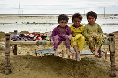 Tres niños de una familia están sentados en un charpai (cama), el 18 de agosto de este año, después de que su comunidad se mudara a un lugar más seguro cuando las inundaciones azotaron su aldea en el distrito de Naseerabad, provincia de Baluchistán, en Pakistán.