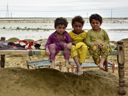 Tres niños de una familia están sentados en un charpai (cama), el 18 de agosto de este año, después de que su comunidad se mudara a un lugar más seguro cuando las inundaciones azotaron su aldea en el distrito de Naseerabad, provincia de Baluchistán, en Pakistán.