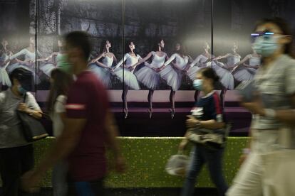 Un grupo de personas con mascarilla pasa delante de un cartel con bailarinas de ballet, en el metro de Hong Kong.