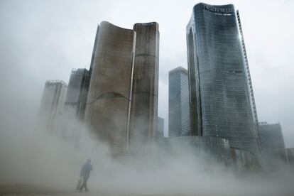 Un hombre camina a través de una nube de polvo cerca de los rascacielos de oficinas recién erigidos en Pekín, China.