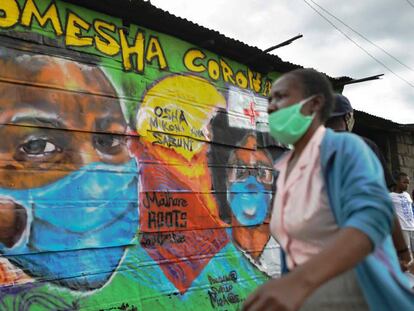 Una mujer con mascarilla pasa por delante de una pintura mural en la que se lee 'Komesha Corona' ("Acabemos con el corona", en suajili) en el barrio de Mathare de la capital de Kenia, 29 de abril de 2020.