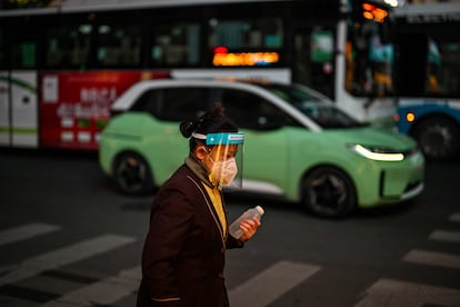 Una mujer con mascarilla y pantalla protectora pasea por el barrio de Huangpu en Shanghái (China).