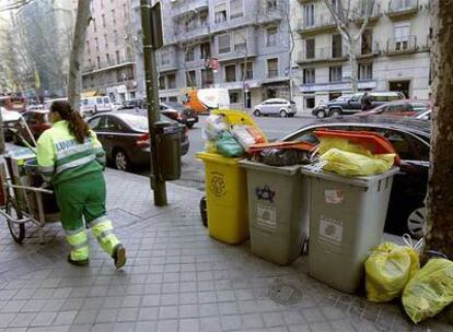Una limpiadora del Ayuntamiento de Madrid pasa junto a varios contenedores repletos de bolsas en una calle del centro.