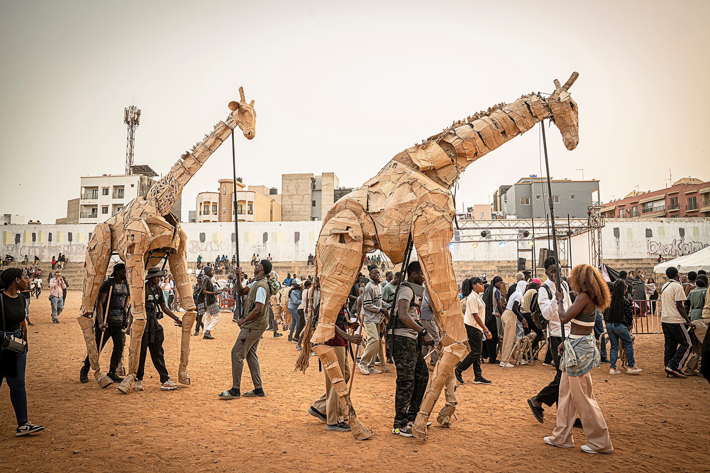 Marionetas de tamaño natural de jirafas, ñus, elefantes o gorilas hechas con cartón desfilaron por las calles del barrio de Ouakam en Dakar, una parada importante en su viaje desde el Congo hasta Noruega. “Dakar es una ciudad de transición, es la ciudad donde África conecta con el resto del mundo por su posición geoestratégica, así ha sido durante siglos” comenta el escenógrafo. La capital de Senegal también es una de las ciudades más amenazadas por el cambio climático.