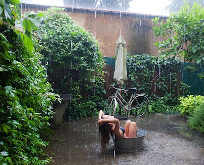 Una mujer disfrutando de una lluvia de verano en su jardín.