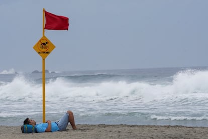 Un turista descansa bajo la bandera roja de alerta ante la cercanía del huracán Agatha a las costas de Puerto Escondido, Oaxaca.