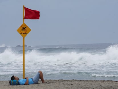 Un turista descansa bajo la bandera roja de alerta ante la cercanía del huracán Agatha a las costas de Puerto Escondido, Oaxaca.