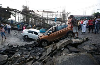 La gente se para junto a los restos de los vehículos atrapados en un puente que colapsó en Calcuta (India).