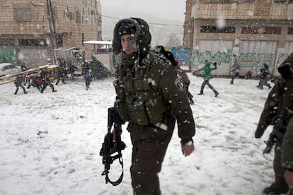 Un policía israelí y jóvenes palestinos que juegan en la nieve en la ciudad de Hebron. En algunas partes de Israel, como en la ciudad de Safed, los colegios han cancelado las clases a causa de la nevada, informa el diario israelí 'Haaretz'.