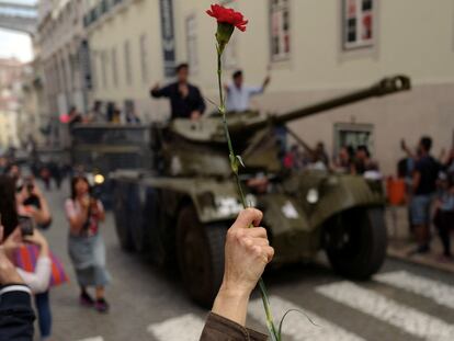 Una persona sostiene un clavel rojo al paso de un vehículo militar original de la revolución de abril, durante la conmemoración del 50 aniversario, este jueves en Lisboa.