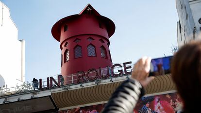 Un viandante fotografía el emblemático molino de viento rojo situado en lo alto del Moulin Rouge, el cabaret más famoso de París, después de que sus aspas se desprendieran durante la madrugada del 25 de abril. 