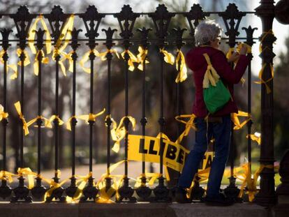 Una mujer coloca lazos amarillos en la verja del Pac de la Ciutadella, donde la ANC ha instalado una pantalla gigante para seguir en directo la sesión constitutiva del Parlament. En vídeo, el PSC se muestra contrario a la investidura de Puigdemont con voto delegado.