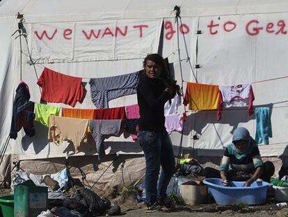Una mujer lava la ropa junto a una tienda con la inscripción en inglés: "Queremos ir a Alemania".
