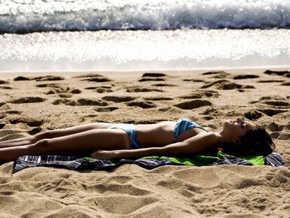 Una mujer toma el sol en la playa, en Barcelona. En el vídeo, información sobre la composición del Sol.