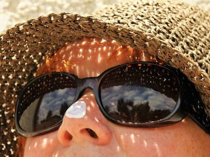 Una mujer toma el sol con algo de crema solar protegiéndole la nariz.