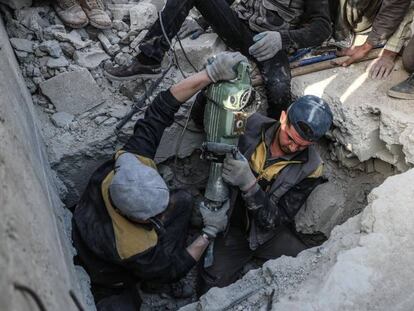 Miembros de Defensa Civil Siria buscan el cuerpo de una víctima bajo un edificio derrumbado en la región de Guta-