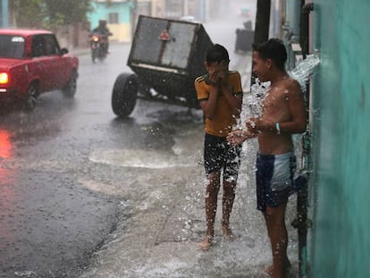 Unos niños se divierten con un chorro de agua mientras llueve en La Habana, Cuba