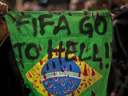 Un manifestantes con una bandera de Brasil en la que se lee "FIFA, vete al infierno".