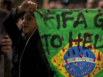 Un manifestantes con una bandera de Brasil en la que se lee "FIFA, vete al infierno".