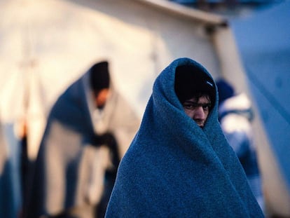 Tres inmigrantes cubiertos con mantas esperan este miércoles un autobús en el punto de registro de Presevo (Serbia).