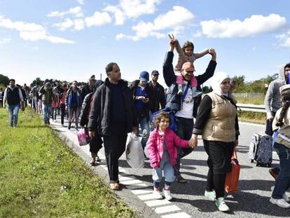 Refugiados, a maioria sírios, caminham por uma estrada da Dinamarca.