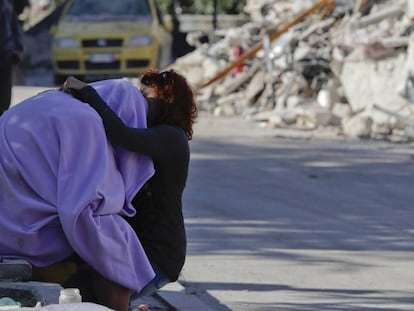 Un hombre y una mujer se consuelan frente a una casa en ruinas. AP