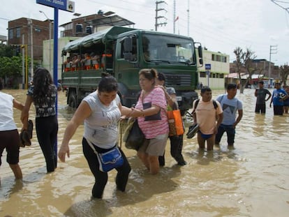 Un grupo de personas intenta cruzar una calle inundada por el río Piura el lunes en Perú.