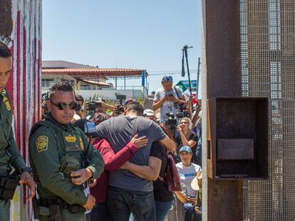 Una familia se abraza en la valla de Tijuana, vigilada por la policía de fronteras.