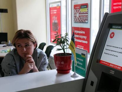 Una empleada de Oschadbank, junto a un cajero afectado por el virus, este martes en Kiev.