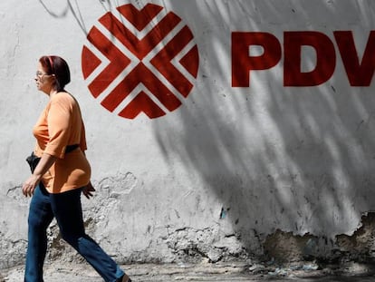 Una mujer camina frente al logo de la petrolera venezolana PDVSA en Caracas. En vídeo, declaraciones de Wilbur Ross.