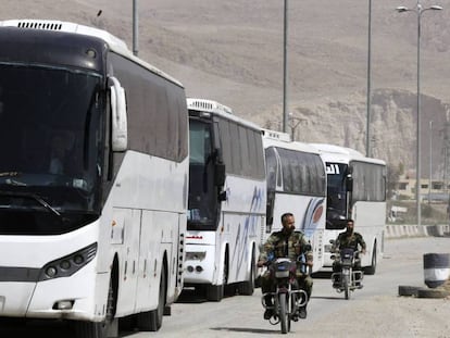 Dos soldados del Ejército sirio patrullan en moto frente a los autobuses que esperan en la entrada de Harasta, en Guta Oriental, este jueves. AFP