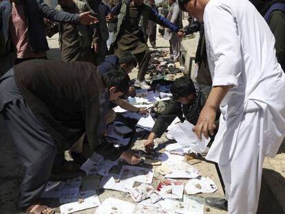 Afganos recogen documentos y fotos de las personas muertas y heridas en el atentado de hoy en Kabul.