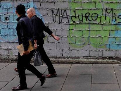 Dos personas caminan este sábado en Caracas por delante de una pintada en la que se lee "Maduro, Miseria".