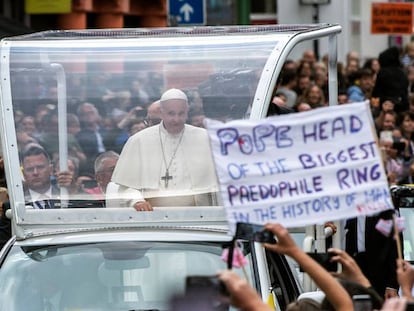 Ativista mostra um cartaz contra o papa Francisco (c), que percorre as ruas do centro de Dublin a bordo do papamóvel, no sábado. No vídeo, o Papa reza em Dublin pelas vítimas dos abusos.