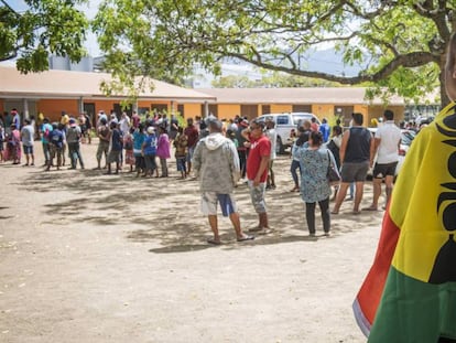 Un hombre, con una bandera de Nueva Caledonia ante un colegio electoral.